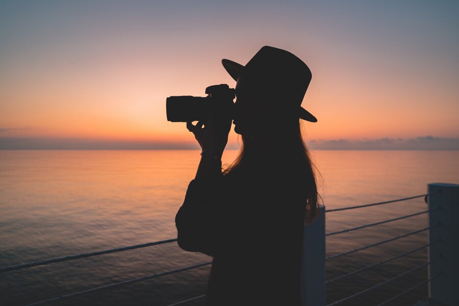 silhueta de um fotografo de mulher de chapeu com camera dslr durante tirar fotos do mar ao por do sol 122732 2206 Click and Play - Agência de Vídeo Digital - Produtora Audiovisual